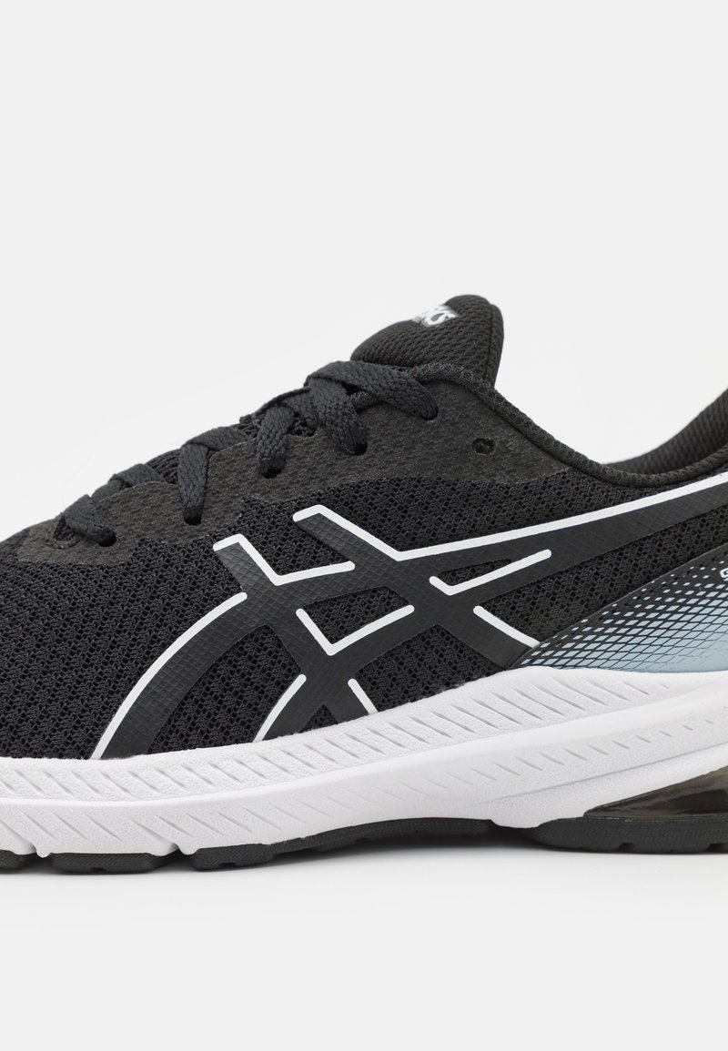 Zapatilla deportiva negra con parte superior de malla, acentos blancos y suela de goma texturizada. Presenta cordones y un diseño con un patrón de degradado.