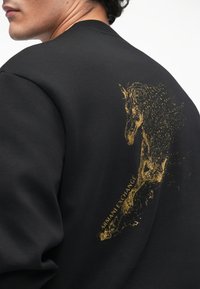 Melna kapuce ar zelta vienradža grafiku un "Armani Exchange" tekstu aizmugurē. Izgatavota no mīksta kapucēšanas auduma.