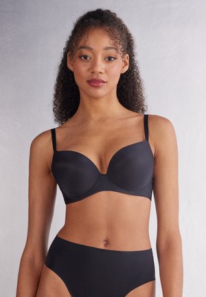 Soutien-gorge noir moulé avec des fines bretelles réglables, texture lisse et support par armatures. Présente un design sans couture et des détails de couture subtils.