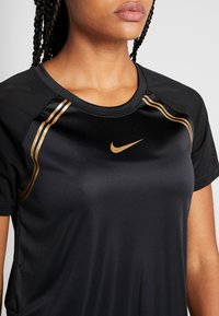 Camiseta atlética negra con textura suave, con detalles en dorado y el logotipo de Nike. Mangas cortas y detalles de malla para ventilación.