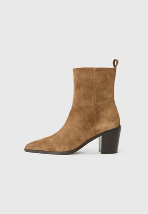 Stivale alla caviglia in suede marrone con punta minuta e tacco spesso nero, presentato su uno sfondo neutro.