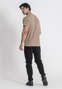 Béžové rebrované tričko s krátkým rukávem spárované s černými slim-fit kalhotami a černými botami. Design obsahuje kulatý výstřih a hladkou texturu.