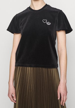 Černý sametový top s krátkými rukávy s nadýchanými rukávy, malým bílým srdcem a logem Adidas na prsou, doplněný olivově zelenou plisovanou sukní.