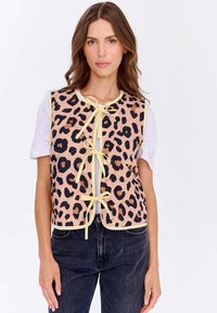 Žena v růžovém a černém svetru s leopardím vzorem, žlutými detaily a mašlemi, pod ním bílé tričko s krátkým rukávem a černé džíny.