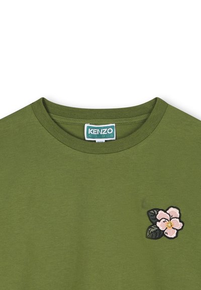 T-shirt en coton vert avec un col rond et une petite broderie florale rose sur la poitrine avec des feuilles vertes.