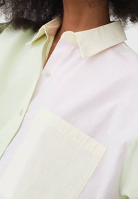 Camicia leggera e multicolore con un design verde pastello e rosa, colletto abbottonato e taschino sulla parte sinistra.