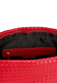 Interno di una borsa a tracolla in pelle intrecciata rossa con fodera in tessuto nero, dotato di una tasca con zip e un piccolo etichetta con lettere in rilievo.