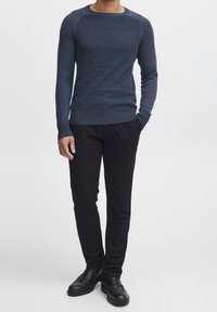 Marineblauer, strukturierter Pullover mit langen Ärmeln und rundem Ausschnitt; kombiniert mit schwarzen, schmal geschnittenen Hosen und schwarzen Slippern.