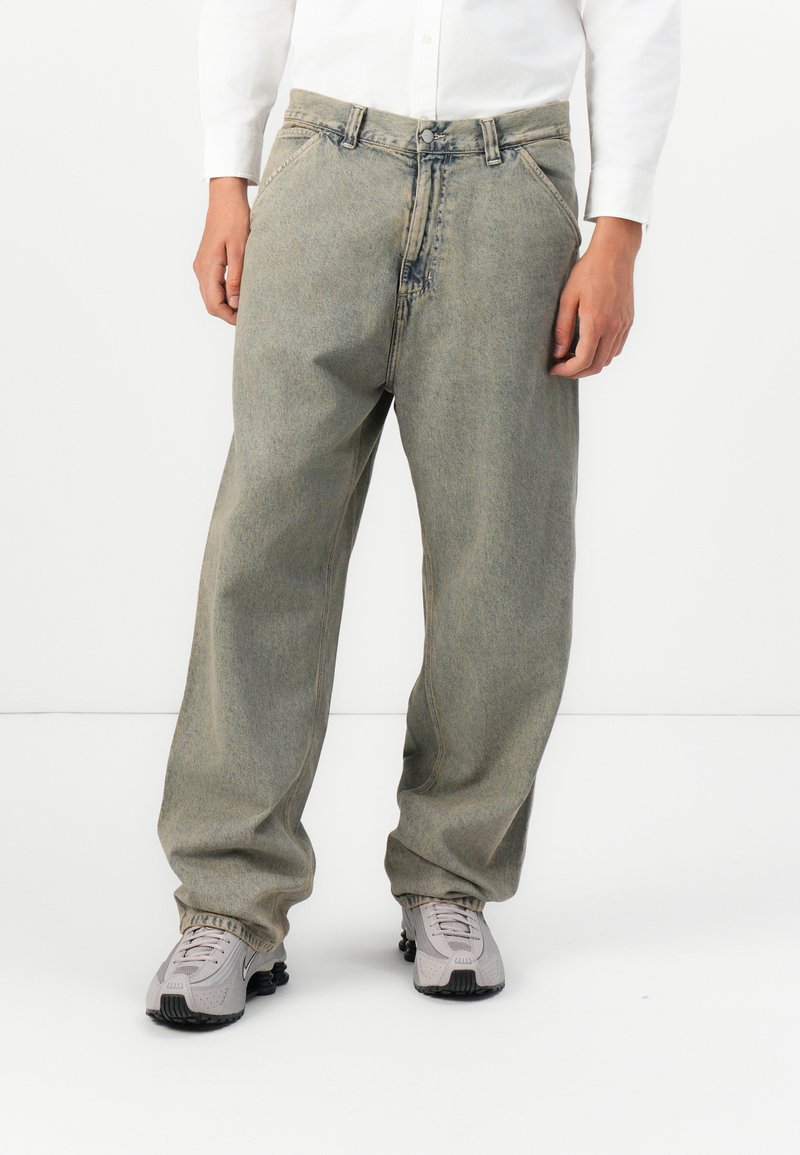 Helle graue baggy Jeans mit hoher Taille. Aus Denim gefertigt, mit geradem Bein, Fronttaschen und Knopfverschluss. Getragen mit grauen Sneakers.