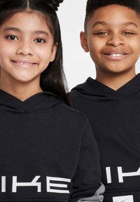 Två barn som bär svarta huvtröjor med vit text på framsidan. Designen inkluderar en grå accent på ärmarna.