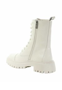 Białe botki za kostkę z błyszczącym wykończeniem, okrągłym noskiem, sznurowanym przodem, bocznym zamkiem błyskawicznym oraz grubą, teksturowaną gumową podeszwą.