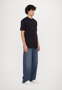 Camiseta de cuello redondo de color marino con un diseño rectangular texturizado en el pecho, combinada con jeans de pierna ancha en azul claro y zapatillas blancas.