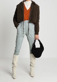 Hnědá kordurová zkrácená bunda, oranžový pletený svetr, mátově zelené přiléhavé kalhoty, bílé boty do kolen, černá kabelka. Hladké textury a vrstvený design.