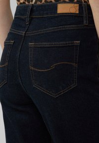 Granatowe dżinsy w dopasowanym kroju, ozdobione złotymi szwami, z dwoma tylnymi kieszeniami oraz skórzaną metką w pasie.