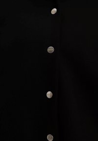 Zwarte gebreide cardigan met zes zilveren knoopsluitsystemen met gegraveerd merk. De stof heeft een soepele, zachte textuur.