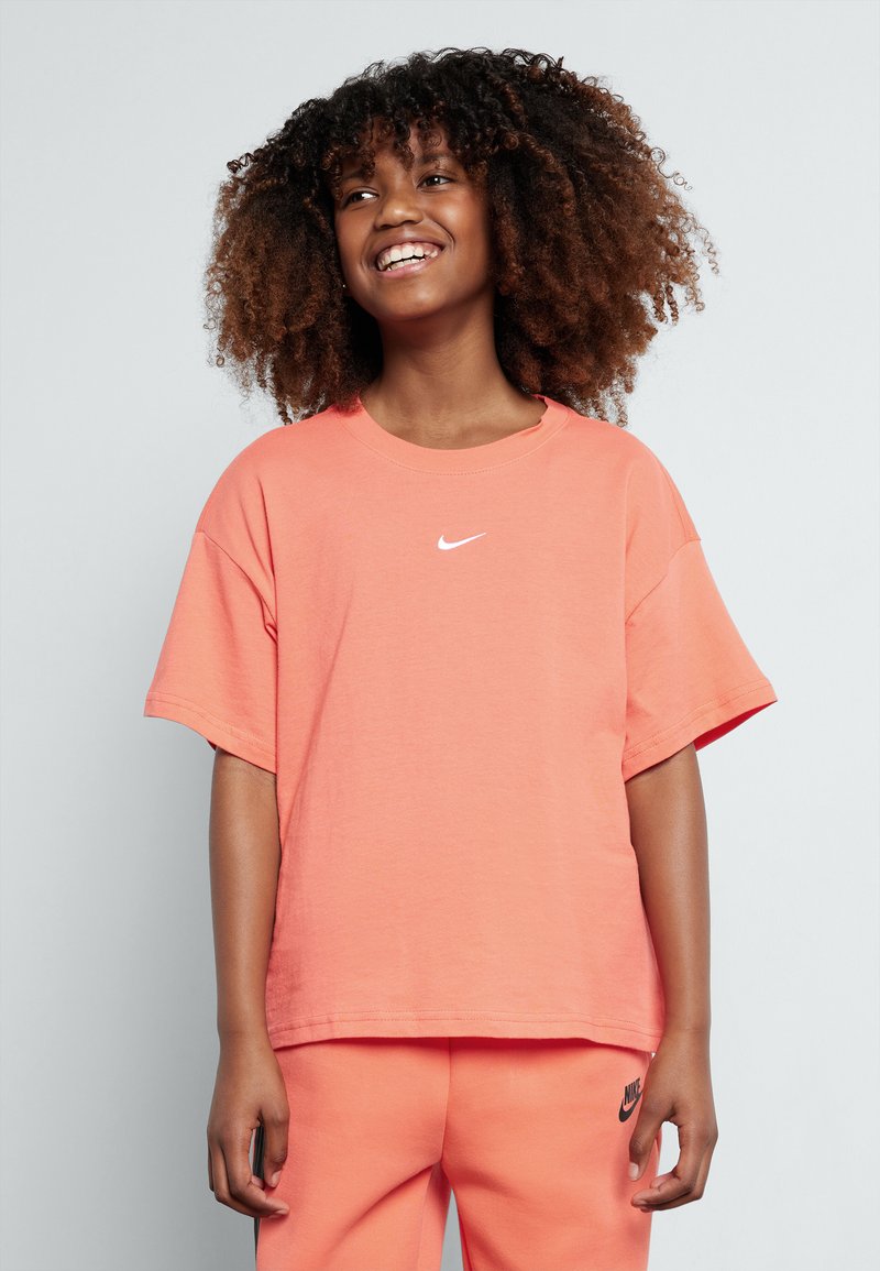 Tricou corai dintr-o țesătură moale, cu o croială lejeră. Prezentă un mic logo alb Nike pe piept. Este asortat cu pantaloni corai.