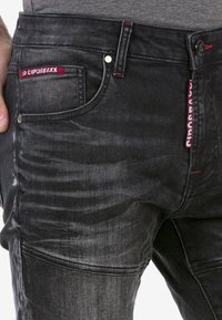 Männer schwarze Denim-Jeans mit einem verblassten Finish, roten Nähakzenten und einem kleinen Logo-Tag an der vorderen Tasche sowie standardmäßigen Taschen.