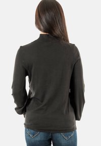 Jersey negro de manga larga con un cuello acanalado y una textura suave, combinado con jeans de mezclilla. Presenta un diseño simple y ajustado.