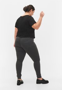 Crna majica kratkih rukava u kombinaciji sa sivim uskim trapericama, s stražnjim džepovima i slim fit krojem. Crne cipele s debelim potplatima. Bijela pozadina.