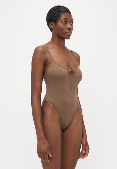 Maillot de bain une pièce marron à côtes, avec des bretelles spaghetti, des côtés découpés et un détail de lien à l'avant. Texture douce et design minimaliste.