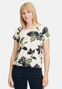 Kremowa bluzka na krótki rękaw w kwiatowy wzór, z granatowymi i oliwkowymi liśćmi. Miękka tkanina o luźnym kroju oraz zaokrąglonym dekolcie.
