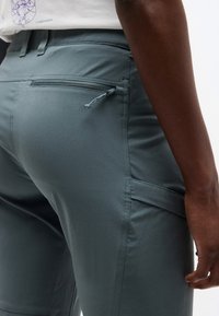 Κοντινό πλάνο προσώπου που φοράει γκρι παντελόνι με φερμουάρ στην πίσω τσέπη, πλαϊνή τσέπη cargo και μέρος λευκού πουκαμίσου ορατό.