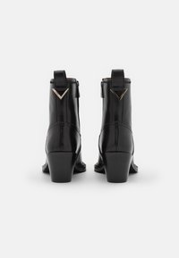 Černé kožené kotníkové boty se zvýšeným podpatkem, se geometrickými akcenty vzadu a hladkým povrchem. Zapínání na zip na boku.