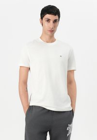 T-shirt en coton blanc à manches courtes avec un petit logo sur la poitrine. Texture lisse et design classique à col rond.