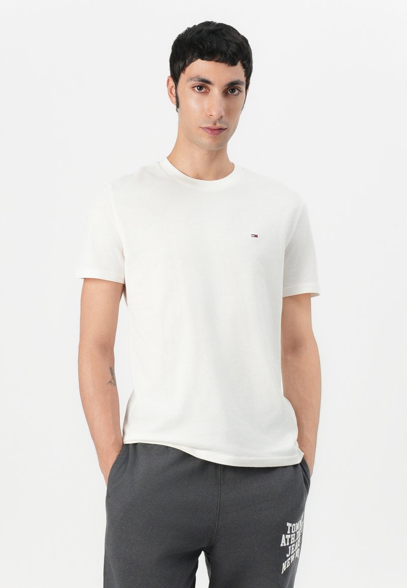 Camiseta de algodón blanca de manga corta con un pequeño logo en el pecho. Textura suave y diseño clásico de cuello redondo.