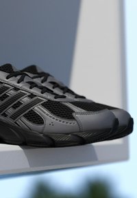 Čierne a sivé športové topánky s vrchnou časťou z priedušnej sieťoviny, s textúrovanými prekrývacími vrstvami, zaoblenou špičkou a vzorovanou podrážkou, vystavené na bielom povrchu.