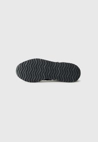 Black rubber shoe sole with a zigzag tread pattern, featuring raised lines for traction and embossed branding on the surface.