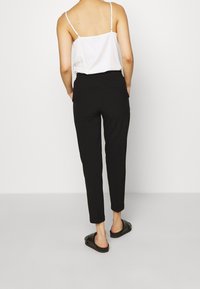 Svarta skräddarsydda byxor med smal passform, ankellängd och elastisk midja. Matcher med en vit topp och svarta slidesandaler.