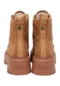 Botas de tobillo de ante marrón con una suela de goma gruesa y texturizada. Presentan una plataforma acanalada, logo de marca en relieve y una pestaña en la parte trasera.