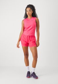 Dámský sportovní outfit obsahující jasně růžový bezrukávový top a odpovídající šortky s texturovaným vzorem. Černé logo Nike na tričku.