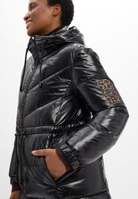 Schwarze Daunenjacke mit glänzender Oberfläche, mit tailliertem Schnitt, Kapuze und Leomuster-Detail am linken Ärmel.