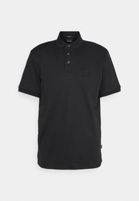 Svart pikétröja i mjuk bomull. Har en krage, tre knappstängningar och en liten svart logotyp på bröstet. Korta ärmar.