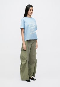 Φωτεινό γαλάζιο βαμβακερό t-shirt με λευκό κείμενο, σε συνδυασμό με χακί χαλαρά παντελόνια cargo, με μεγάλες τσέπες και άνετη εφαρμογή. Μαύρα παπούτσια.