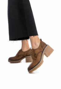 Zapatos de tacón de cuero marrón con dise�ño de cordones, que presentan una suela de goma y costuras en contraste. Tacón grueso y puntera redondeada.