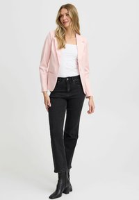Hele roosa puhvblazer, mis on kohandatud sobivusega, on kombineeritud mustade sirgete pükstega. Mustad kontsad täiendavad kui outfit. Pehme materjal ja minimaalne disain.