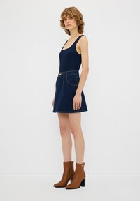 Tummansininen scoop-neck -toppi, joka on yhdistetty tumman denim A-linjan minihelmaan, jossa on taskut ja solkipanta. Ruskeat korkeat nilkkurit.