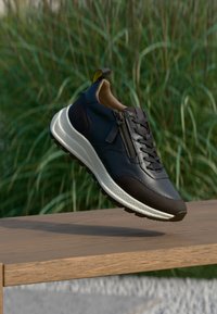 Must tahtsneaker tumed õhuke nahk, tume aktsent ja valge tallaga, millel on tõmblukk. Libisemiskindel tallapind ja pehmendusega disain mugavuseks.