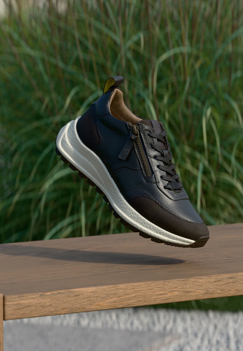 Must tahtsneaker tumed õhuke nahk, tume aktsent ja valge tallaga, millel on tõmblukk. Libisemiskindel tallapind ja pehmendusega disain mugavuseks.