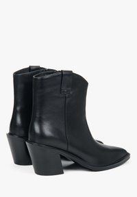 Para czarnych skórzanych botków za kostkę na słupku, z zamkiem błyskawicznym z boku i pętlami do zakupu na białym tle.