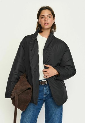Black padded jacket with a high collar, double-breasted buttons, and loose sleeves. Paired with blue jeans and a brown suede bag.