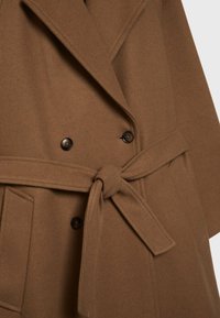 Manteau en mélange de laine marron avec un design à double boutonnage, de gros boutons, une taille ceinturée et des poches à rabat. Texture douce et forme structurée.