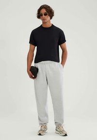 Schwarzes T-Shirt mit kurzen Ärmeln, kombiniert mit grauen Jogginghosen. Das Outfit besticht durch eine entspannte Passform, weichen Stoff und Turnschuhe mit einem markanten Design.