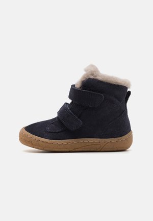 Chaussure montante en daim marine pour enfants avec deux bandes Velcro, doublure en fourrure beige et semelle en caoutchouc marron clair.
