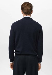 Maglione blu scuro con scollo rotondo e polsini a costine, indossato sopra pantaloni neri, che mostrano una texture liscia.