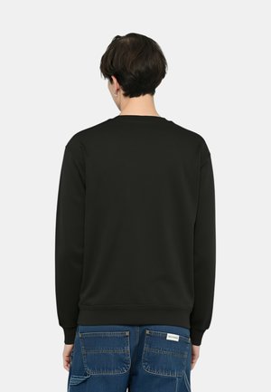 Felpa nera con scollo tondo, maniche lunghe e polsini a costine, realizzata in un materiale liscio; indossata con jeans di denim blu.