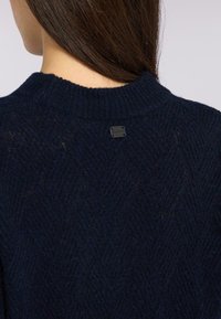 Granatowy sweter dziany z teksturowanym wzorem w warkocz, z prążkowanym okrągłym dekoltem i małą czarną metką logo z tyłu.